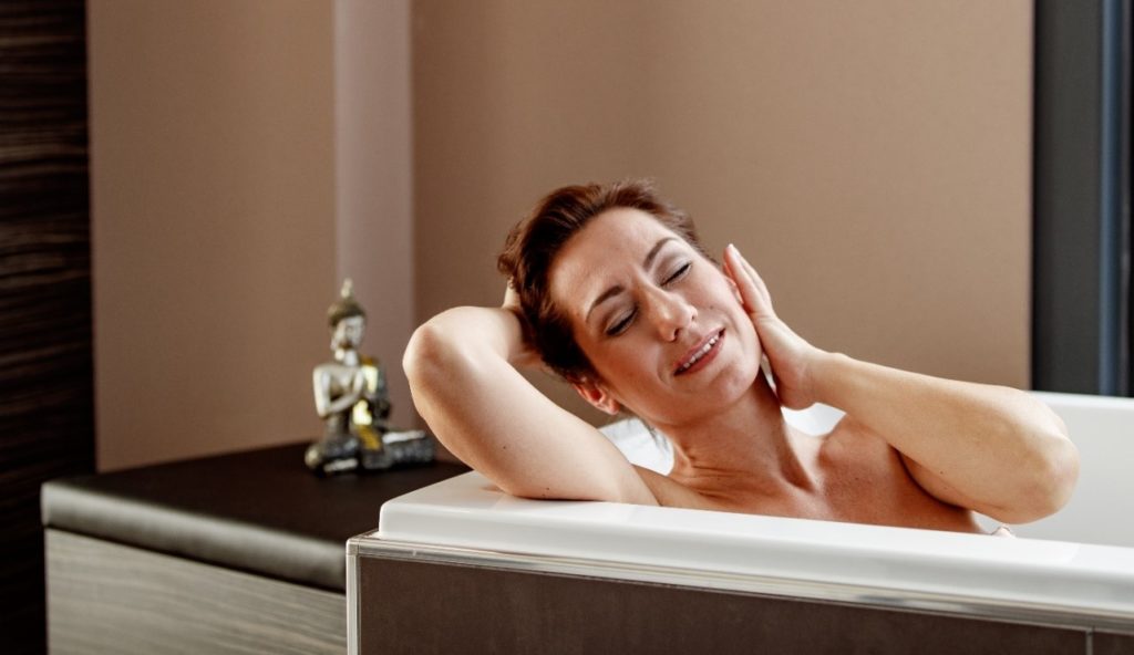 Frau liegt in der Badewanne und streicht sich über das Gesicht
